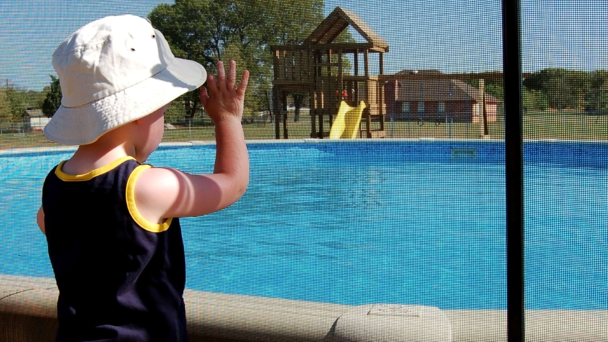 A child looking at a swimming pool through a safety fence