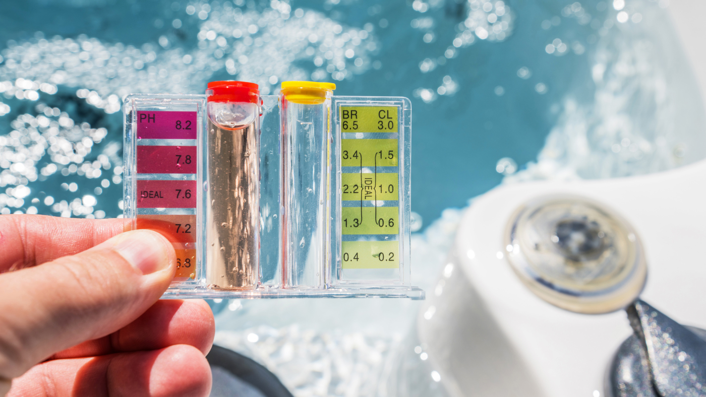 a hand holding a water testing kit above the surface of an active hot tub